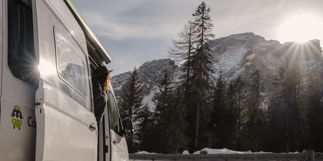 Frau schaut aus VW Grand California Campervan vor Bergen im Schnee