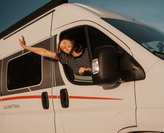 A woman is sticking her head and arm out of the camper window