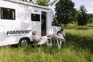 People are relaxing by the camper while drinking coffee